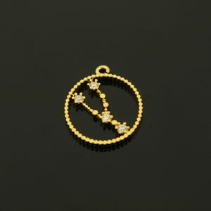 May include: Gold-toned pendant charm featuring a constellation design with clear rhinestones. The pendant is circular and has a beaded edge.