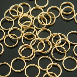 Könnte beinhalten: Ein großer Haufen goldfarbener Metall-Sprünge. Die Ringe sind alle gleich groß und in einem zufälligen Muster angeordnet.