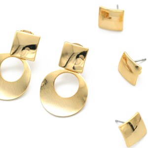 May include: A pair of gold earrings with a round shape and a square accent. The earrings are made of a brushed metal and have a modern design.