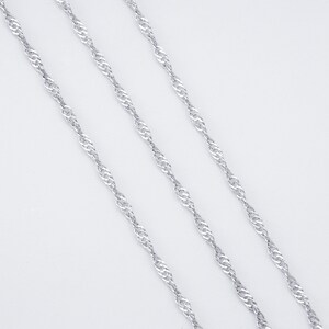 Peut inclure: Trois chaînes argentées, chacune d'une longueur différente, sont disposées sur une surface blanche. Les chaînes sont de conception torsadée, ressemblant à une corde.