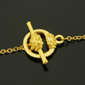 May include: Gold-toned toggle clasp with a decorative floral design. The clasp is attached to a gold chain.