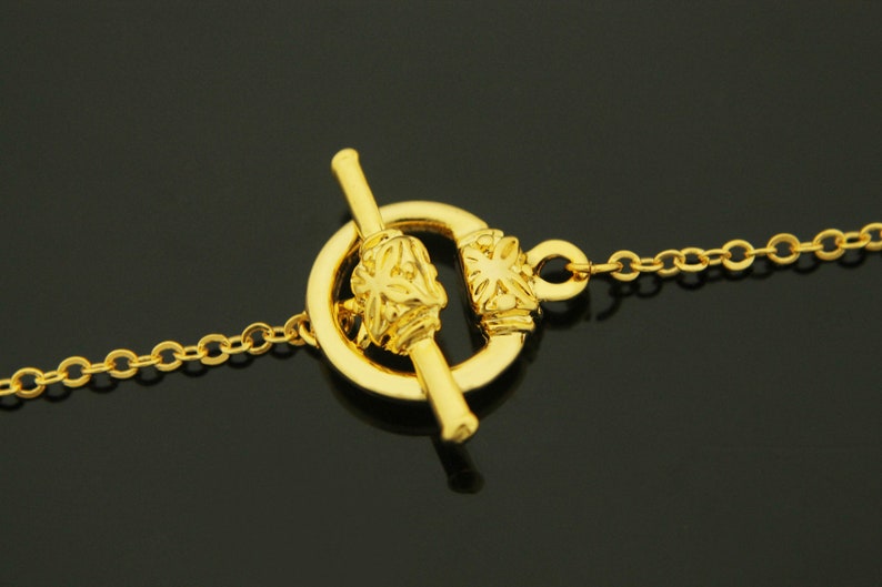 May include: Gold-toned toggle clasp with a decorative floral design. The clasp is attached to a gold chain.