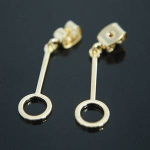 Puede incluir: Un par de pendientes de oro con un pequeño colgante circular que cuelga de cada uno. Los pendientes tienen un diseño sencillo y son perfectos para el uso diario.