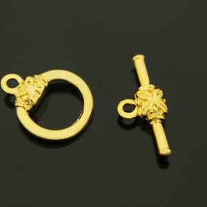 May include: Gold-toned metal clasp with a decorative floral design. The clasp has a ring on one end and a toggle bar on the other end.