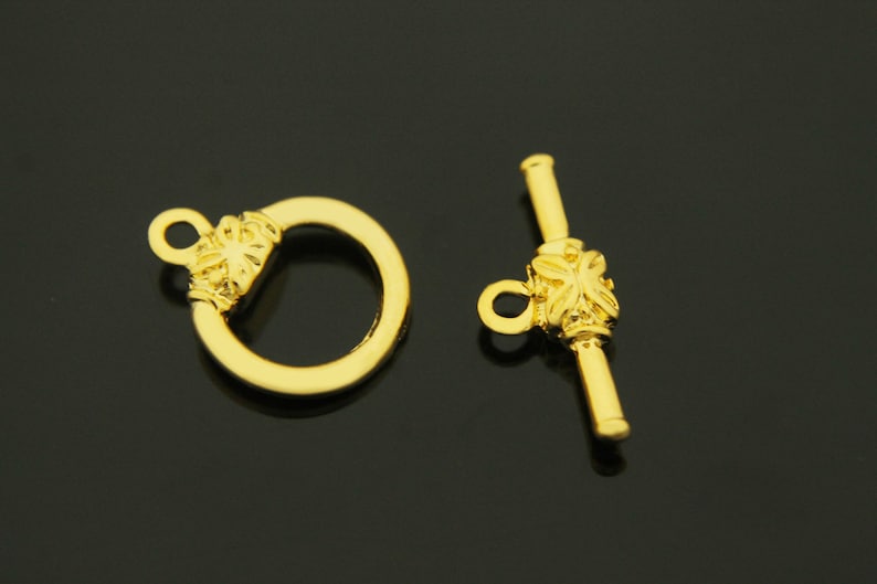 May include: Gold-toned metal clasp with a decorative floral design. The clasp has a ring on one end and a toggle bar on the other end.