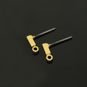 May include: A pair of gold-tone earring posts with a small rectangular charm and a loop at the bottom.
