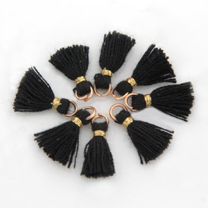 May include: Eight black tassels with gold accents and a copper ring. The tassels are arranged in a circle on a white background.
