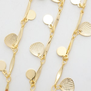 Könnte beinhalten: Goldene Kettenkette mit mehreren baumelnden Anhängern. Die Anhänger sind rund und muschelförmig. Die Kette ist zart und hat ein wellenförmiges Design.
