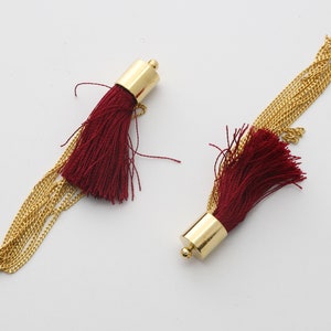 May include: Two burgundy tassel earrings with gold chain accents. The tassels are made of soft, fine threads and the chains are delicate and shiny.