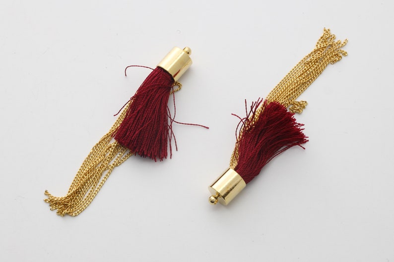 May include: Two burgundy tassel earrings with gold chain accents. The tassels are made of soft, fine threads and the chains are delicate and shiny.