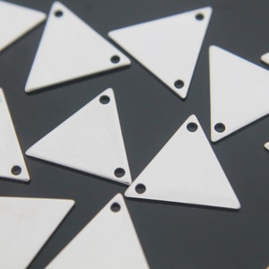 May include: A group of white metal triangle shapes with two holes each. The triangles are scattered on a black surface.
