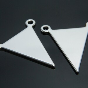 Puede incluir: Dos abalorios de metal de forma triangular plateados con tres anillos de salto cada uno. Los abalorios son planos y tienen un acabado liso y pulido.