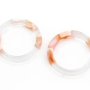May include: Two clear plastic rings with a marbled pattern in shades of pink and peach.