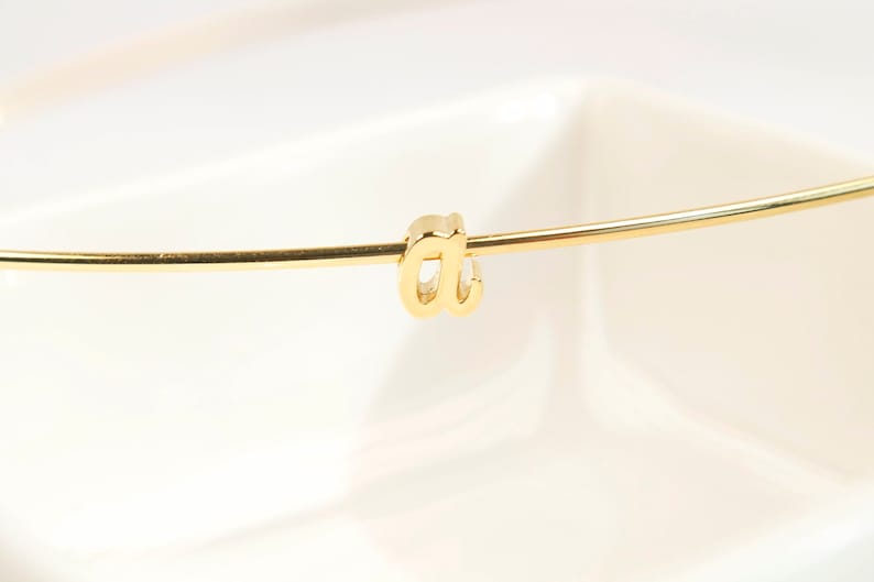 Puede incluir: Una pulsera dorada con un solo dije con la letra 'a'.