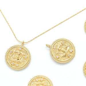 May include: Gold necklace with multiple charms featuring a detailed design of a figure holding a scale. Each charm is adorned with small, clear rhinestones.