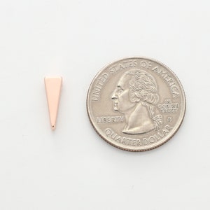May include: A small, rose gold triangle charm, approximately the size of a US quarter.