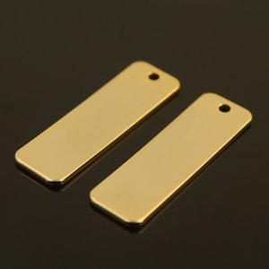 May include: Two gold-colored metal rectangular tags with a hole at the top.