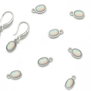 Puede incluir: Un conjunto de diez dijes ovalados de plata con piedras de ópalo blanco. Los dijes tienen un bucle en la parte superior para sujetarlos a joyas.