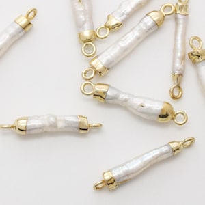 May include: A collection of white, oblong pearl beads with gold-colored metal accents. Each bead has a gold cap on each end with a small loop for stringing. The pearls are irregularly shaped, giving them a natural appearance.
