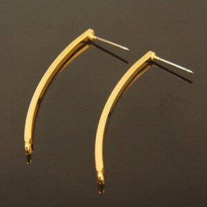 Puede incluir: Un par de pendientes de color dorado con forma alargada y curvada. Los pendientes tienen un diseño simple y minimalista.