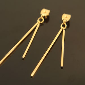 May include: A pair of gold-toned dangle earrings with two thin, straight bars hanging from each earring.