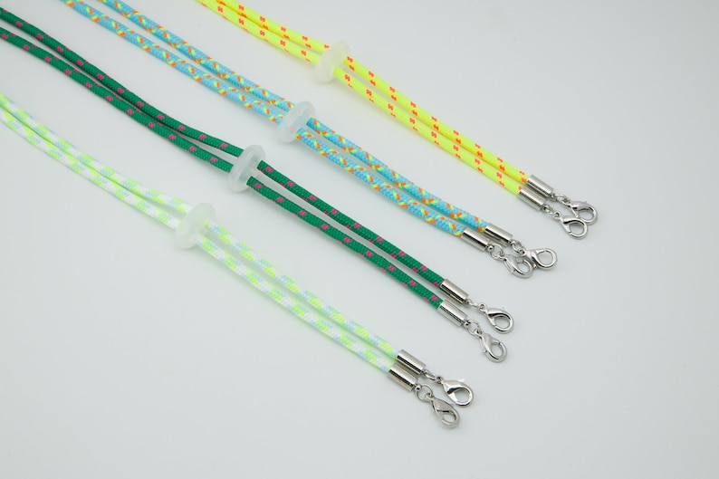 May include: Four colorful mask lanyards with adjustable length and silver clasps. The lanyards are green with pink dots, blue with orange dots, yellow with red dots, and white with green dots.
