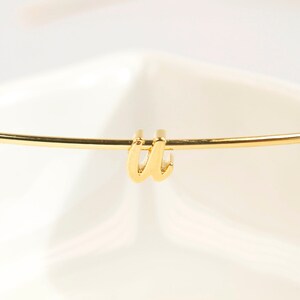 May include: A gold-coloured initial 'W' charm attached to a thin gold-coloured bangle bracelet.