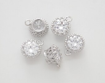 May include: Five silver-toned metal charms with clear rhinestone accents. Each charm features a round rhinestone surrounded by a decorative border. The charms have a loop at the top for attaching to jewelry or other crafts.