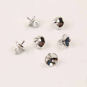 May include: Five silver-toned metal bead caps with a loop on one side and a small hole on the other side. The caps are designed to be used with beads to create jewellery.