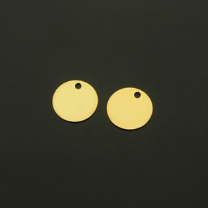 Puede incluir: Dos círculos de metal de color dorado con un pequeño agujero en el centro. Los círculos están sobre un fondo negro.