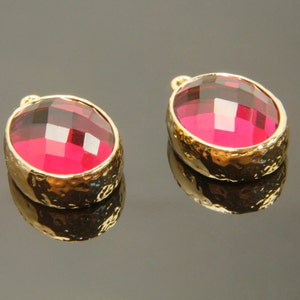 Könnte beinhalten: Zwei ovale rosafarbene Kristallanhänger mit goldenen Einstellungen. Die Anhänger haben ein facettierten Design und sind in einem strukturierten goldenen Rahmen gefasst.