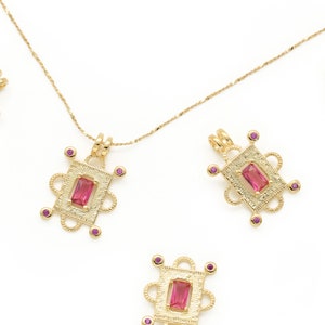 May include: A gold chain necklace with multiple pink gemstone pendants. Each pendant is a square with intricate detailing and a pink gemstone in the center.