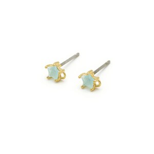 Op de afbeelding: Een paar gouden oorbel studs met lichtblauwe vierkante stenen.