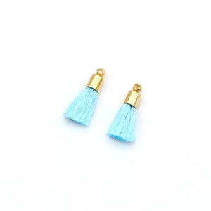 May include: Two light blue tassels with gold metal tops. The tassels are approximately 5 cm long.