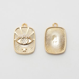 May include: Two gold-colored rectangular charms. One charm features an eye design with a star and a halo of rays, and the other charm has a sunburst pattern. Both charms have a loop at the top for attaching to jewelry.