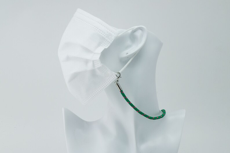 May include: A white face mask with a green and pink patterned lanyard. The lanyard has silver clasps to attach to the mask.