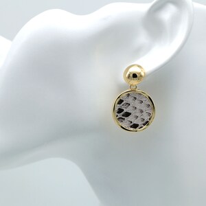 May include: Gold tone drop earrings with a round, white and brown snakeskin patterned design.