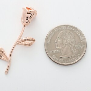 May include: Rose gold rose charm pendant with a single leaf on each side. The charm is shown next to a US quarter for size comparison.