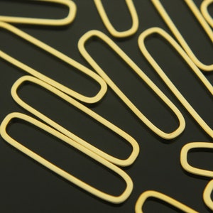 May include: A close-up of a group of gold-colored metal jump rings. The rings are oval-shaped and have a smooth, polished finish.