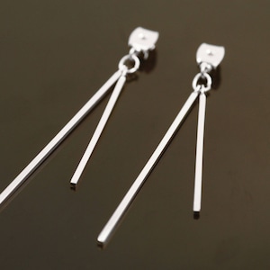 May include: A pair of silver dangle earrings with two thin, straight bars hanging from each earring.