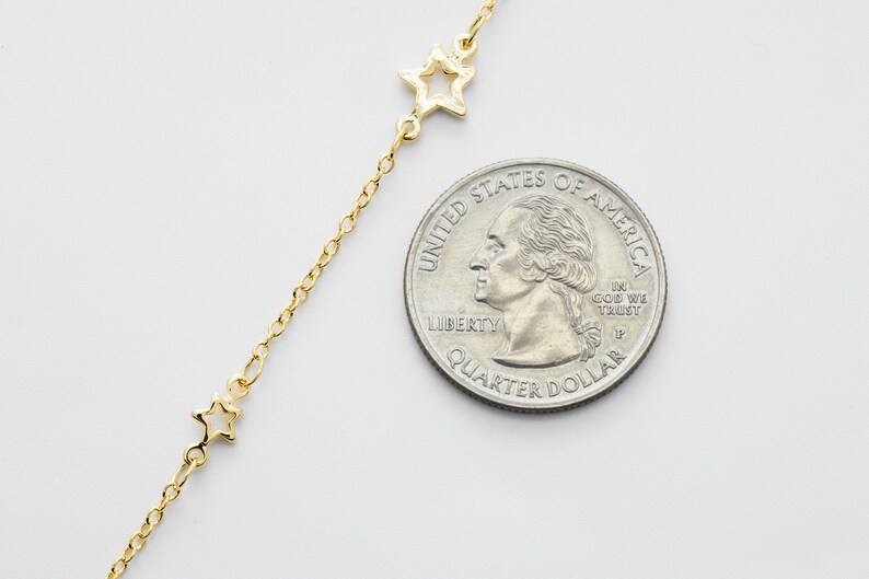 May include: A gold chain necklace with a delicate star charm. The necklace is shown next to a US quarter for size reference.