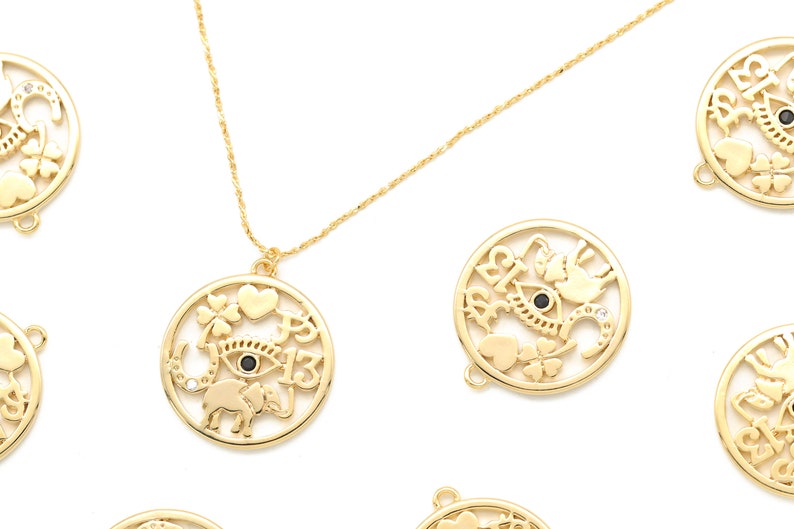 May include: Gold-colored necklace with a round pendant featuring an eye, elephant, heart, four-leaf clover, and the number 13. The pendant is surrounded by a circular frame. Additional gold pendants with similar designs are scattered around.
