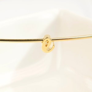 May include: A gold bangle bracelet with a letter 'E' charm.
