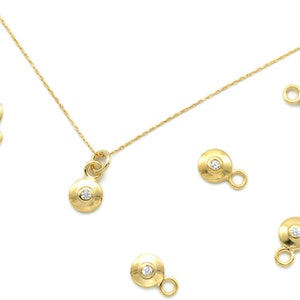 May include: A gold necklace with a small diamond pendant and five additional charms, each featuring a small diamond set in a round gold disc.