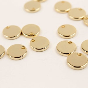 May include: A collection of gold-colored metal circle charms with a small hole in the center. The charms are scattered on a white surface.