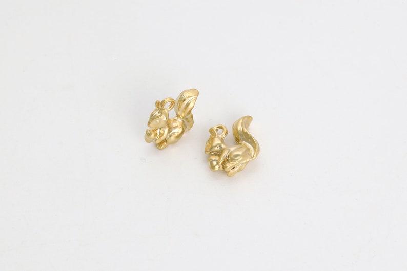 May include: Two gold-colored squirrel charms with a detailed design. The squirrels are holding nuts in their paws.