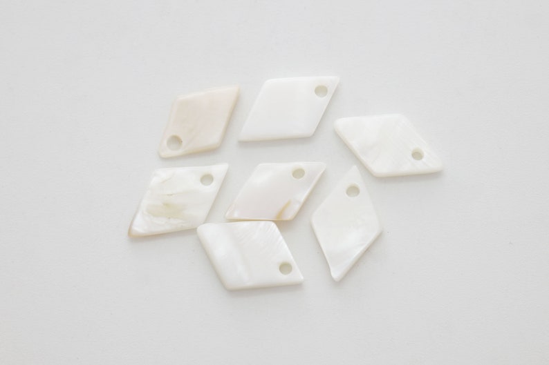 May include: Eight white diamond-shaped shell charms with holes for stringing. The charms have a natural, iridescent sheen.