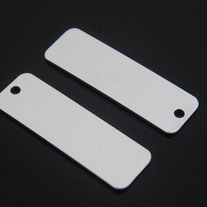 May include: Two blank silver rectangular metal tags with a hole at the top for hanging.