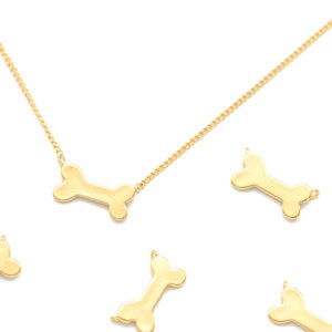 May include: A gold chain necklace with a gold bone pendant. There are several other gold bone charms scattered around the necklace.