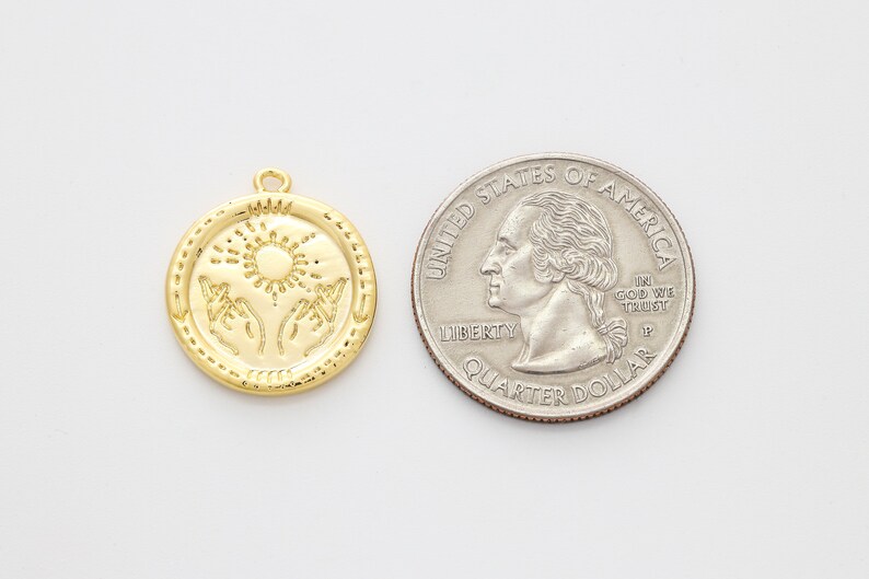May include: Gold-toned pendant charm featuring a sun and two hands reaching up. The charm is about the size of a US quarter.
